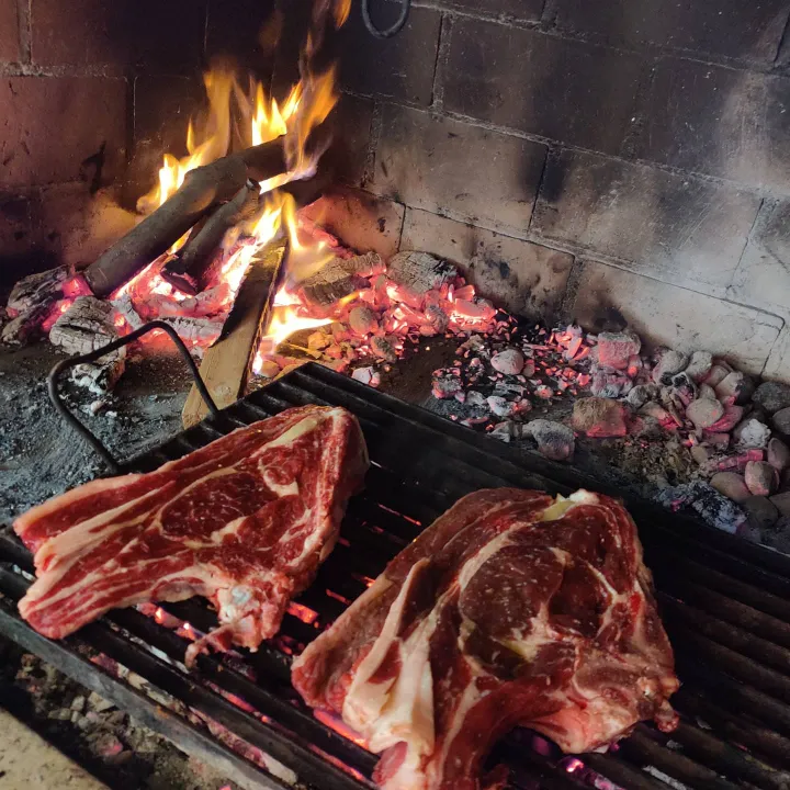 Dikke ribeyes op rooster boven gloeiende kolen in open vuurhaard