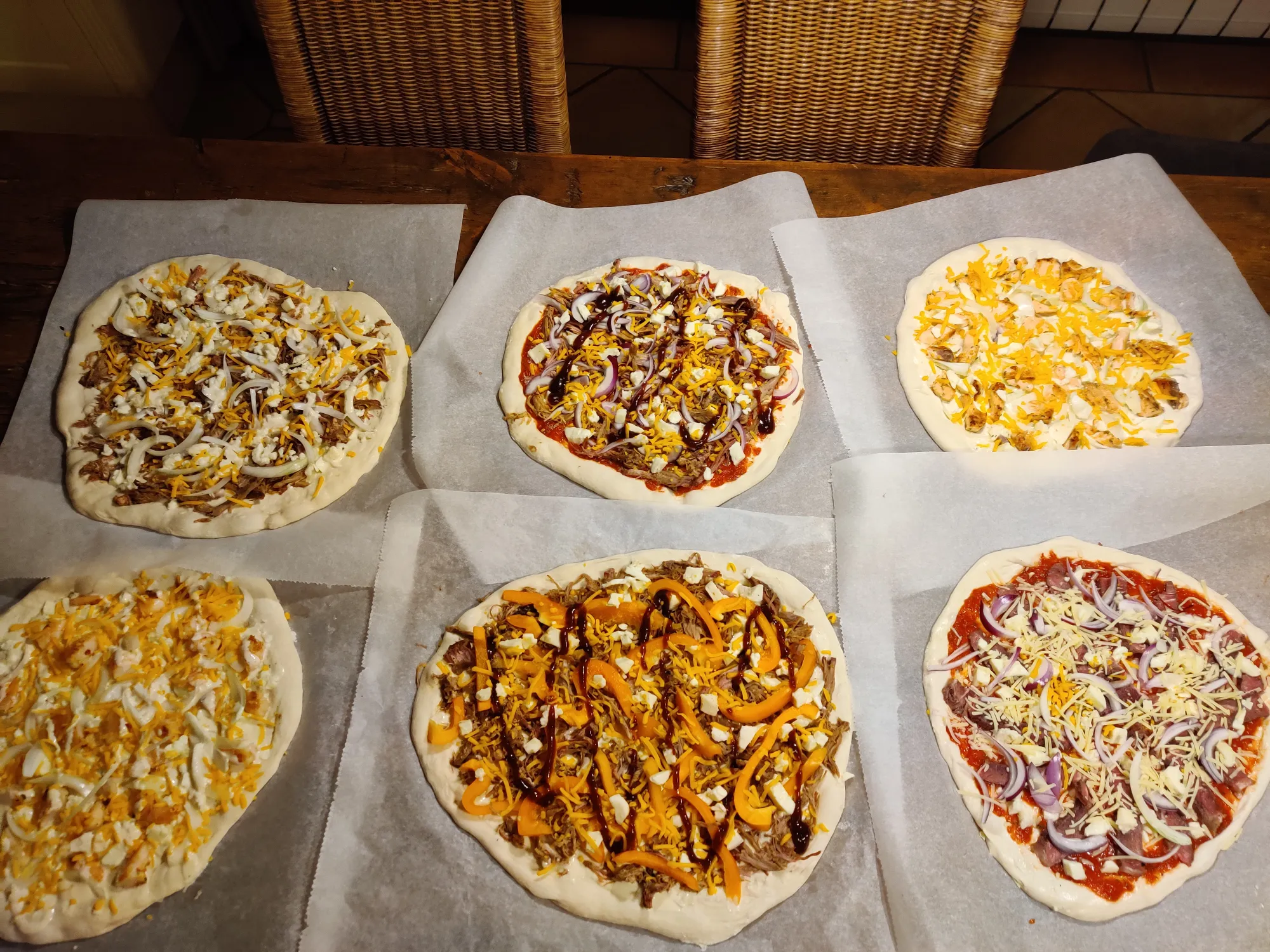 Zes BBQ-pizza's op bakpapier klaar om te grillen — verschillende toppings