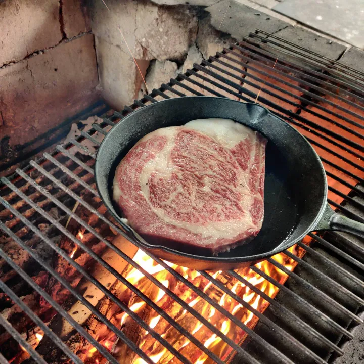 Japanse wagyu ribeye in gietijzeren pan op open vuur — hoge directe hitte